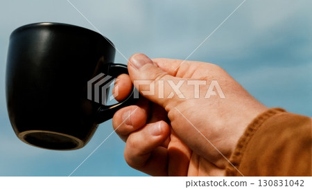 A close-up of a person's hand holding a cup of coffee. Coffee break, a moment of reflection, business pause 130831042