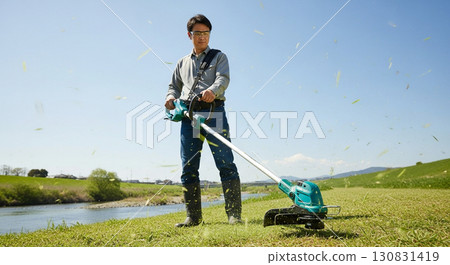 Male worker mowing the grass with a lawnmower 130831419