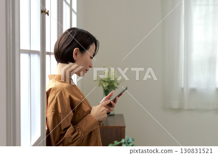一個在窗邊操縱智能手機的女人 一個在窗邊操縱智能手機的女人 130831521