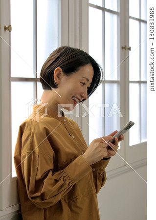 觀看智能手機的婦女在窗口邊 130831988