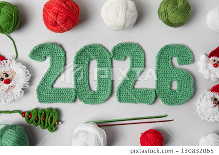 Crocheted toys Santa Claus in red hat, green Christmas tree with balls of thread and crochet hook on gray background. Baby stuff and accessories. Gift for winter holidays. Top view, flat lay. 130832065