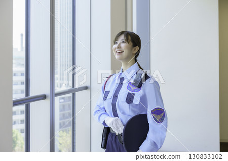 Portrait of a young female security guard standing by a window. Photo courtesy of Tokyo Electronics College, Denpa Gakuen School Corporation. 130833102