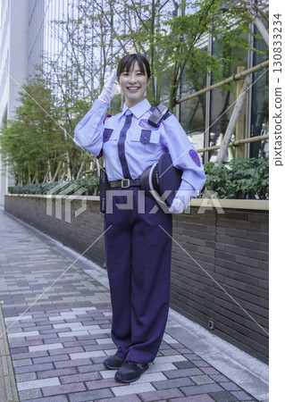 A young female security guard saluting in front of an office building. Vertical. Photo courtesy of Tokyo Electronics College, Denpa Gakuen Corporation. 130833234