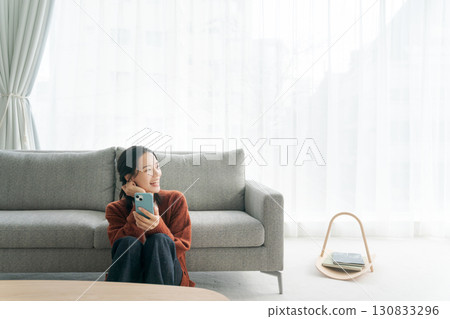 A young woman sitting on a sofa and operating a smartphone 130833296