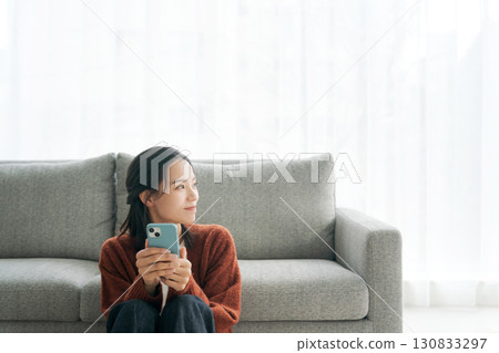 一個年輕的女人，在客廳裡操作智能手機 130833297