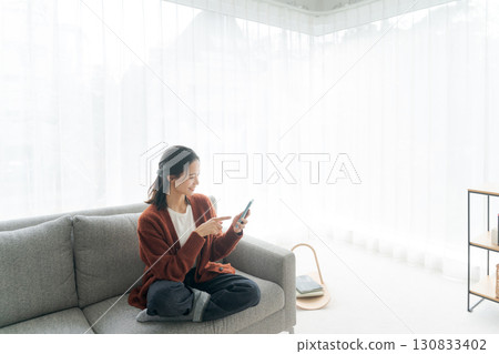 A young woman sitting on a sofa and operating a smartphone 130833402