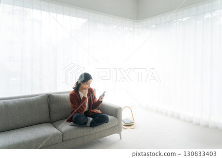 A young woman sitting on a sofa and operating a smartphone A young woman sitting on a sofa and operating a smartphone 130833403