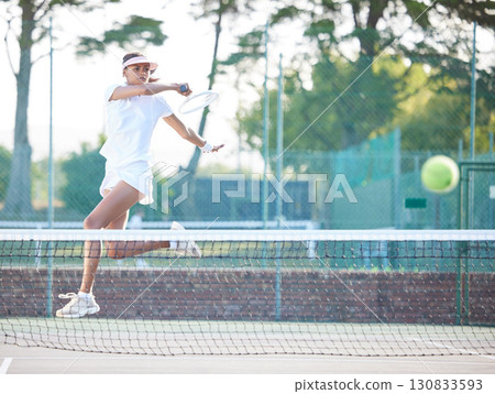 Tennis, outdoor match and woman hit a sports ball with a racket service on a exercise court. Sport game, workout competition and young female doing cardio action for wellness and health in summer 130833593