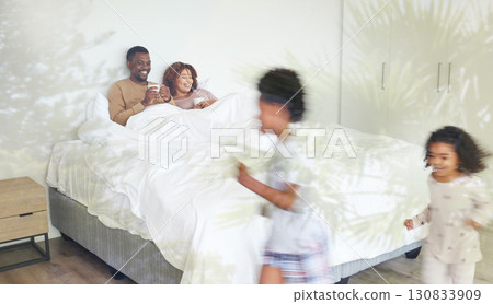 Relax, family and children being playful in the bedroom while their parents lay in bed with a cup of coffee. Happy, love and young couple drinking a cappuccino while watching their kids run together. 130833909