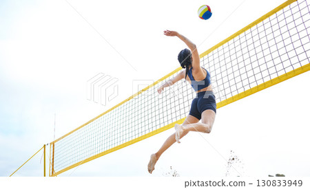 Sports, volleyball and woman jump at beach to hit ball in competition, game or match. Training, exercise and female athlete jumping for spike in tournament for workout, fitness and health at seashore 130833949