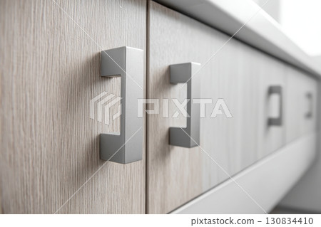 Pair of silver metal cabinet door handles on light wood cabinets. Both handle design. Front kitchen wooden cabinet door and drawers. Closeup furniture base set. Trendy interior units. Home improvement 130834410