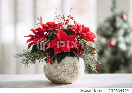Poinsettia plant in a pot. Christmas Star flower. Festive red and golden holiday background with decorations and presents. The background is blurred. Traditional Xmas winter festive red flowers. 130834419