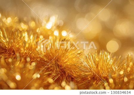 Gold tinsel decoration on a blurred bright golden color background. Close-up, macro. shiny and festive. Christmas glittering, golden and white, shimmering in the light backdrop. New Year's concept. 130834634