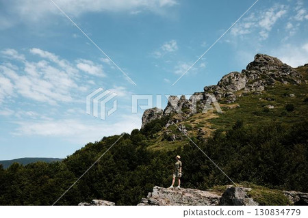 A young woman stands on a cliff in Stara Planina National park, Serbia country, admiring vast green mountains under a blue sky. A perfect moment of freedom and adventure in nature A young woman stands on a cliff in Stara Planina National park, Serbia country, admiring vast green mountains under a blue sky. A perfect moment of freedom and adventure in nature 130834779
