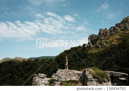 A young woman stands on a cliff in Stara Planina National park, Serbia country, admiring vast green mountains under a blue sky. A perfect moment of freedom and adventure in nature A young woman stands on a cliff in Stara Planina National park, Serbia country, admiring vast green mountains under a blue sky. A perfect moment of freedom and adventure in nature 130834781