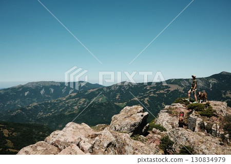 Woman with two dogs German and Australian Shepherd standing on rocky cliffs of Stara Planina, overlooking vast mountain valleys and dramatic landscapes. Travel and hiking with pets concept 130834979