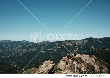 Woman with two dogs German and Australian Shepherd standing on rocky cliffs of Stara Planina, overlooking vast mountain valleys and dramatic landscapes. Travel and hiking with pets concept Woman with two dogs German and Australian Shepherd standing on rocky cliffs of Stara Planina, overlooking vast mountain valleys and dramatic landscapes. Travel and hiking with pets concept 130834986