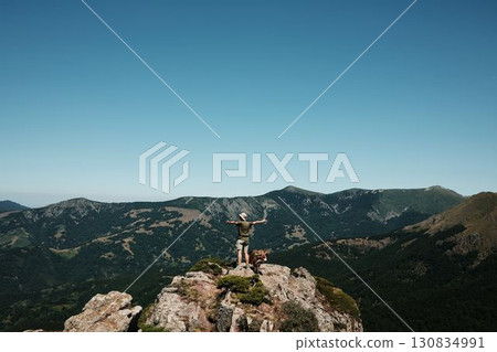 Woman with two dogs German and Australian Shepherd standing on a rocky peak of Stara Planina, enjoying panoramic mountain views under a clear blue sky. Rear view. Travel and hiking with pets concept Woman with two dogs German and Australian Shepherd standing on a rocky peak of Stara Planina, enjoying panoramic mountain views under a clear blue sky. Rear view. Travel and hiking with pets concept 130834991