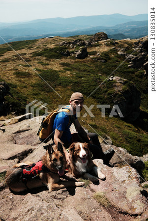 Smiling male hiker with backpack resting on a rock with two dogs German and Australian Shepherd in Stara Planina mountains. Travel and hiking with pets concept Smiling male hiker with backpack resting on a rock with two dogs German and Australian Shepherd in Stara Planina mountains. Travel and hiking with pets concept 130835014