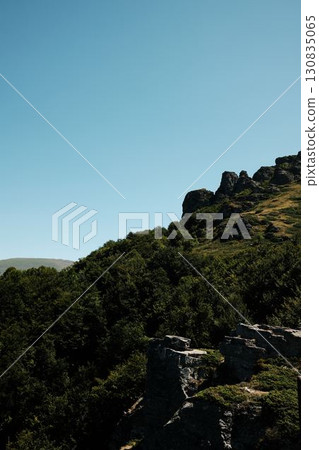 Rugged rocky peaks of Babin Zub mount in Stara Planina rising above lush green hills under bright summer sky. Serbia country Rugged rocky peaks of Babin Zub mount in Stara Planina rising above lush green hills under bright summer sky. Serbia country 130835065