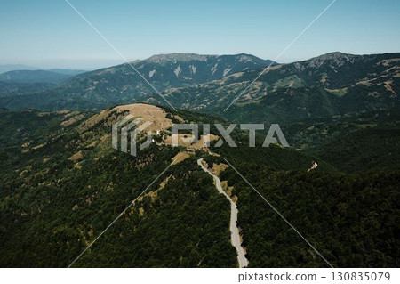 Aerial view of winding road through Stara Planina mountains with golden fields and lush green forests under a clear blue sky. Serbia country Aerial view of winding road through Stara Planina mountains with golden fields and lush green forests under a clear blue sky. Serbia country 130835079