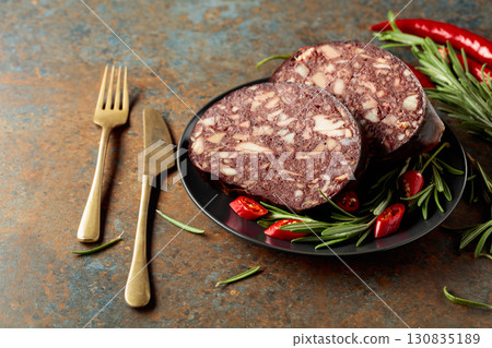 Spanish black pudding or blood sausage accompanied by rosemary and red pepper on a black plate. Spanish black pudding or blood sausage accompanied by rosemary and red pepper on a black plate. 130835189
