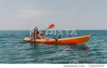 Kayaking Woman Ocean Paddle - A woman paddles a bright orange kayak on a calm, blue ocean. 130835437