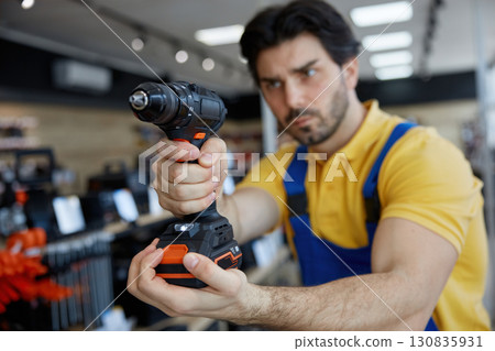 A man worker in work clothes is holding a drill A man worker in work clothes is holding a drill 130835931