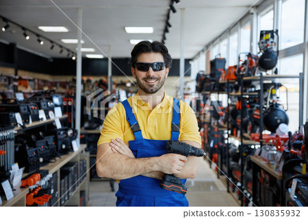 A man worker in stylish sunglasses, is holding a drill in a store A man worker in stylish sunglasses, is holding a drill in a store 130835932