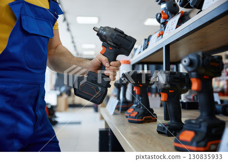 A man is holding a black and orange handheld drill in both hands A man is holding a black and orange handheld drill in both hands 130835933