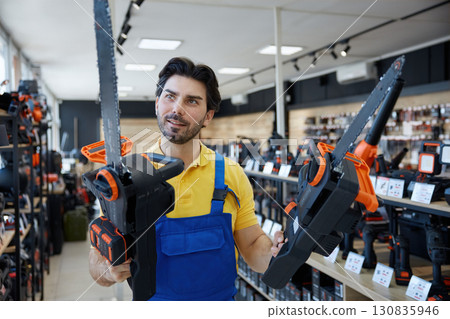 A man is standing in a store holding a chainsaw tool A man is standing in a store holding a chainsaw tool 130835946