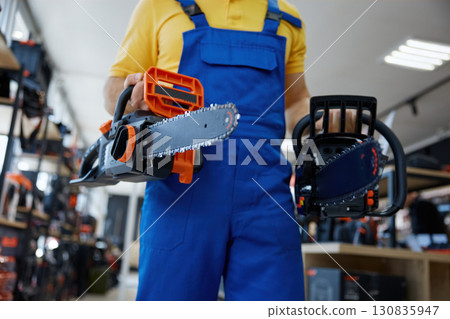 A man worker holding two chainsaws inside a store 130835947