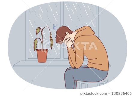 Depressed man sits alone and suffers from melancholy in room with window and wilted flower 130836405