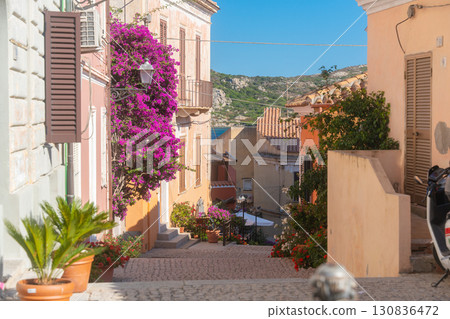 Picturesque view of a Mediterranean alley adorned with colorful bougainvillea and charming pastel buildings. Greenery and traditional architecture create a serene and inviting atmosphere 130836472