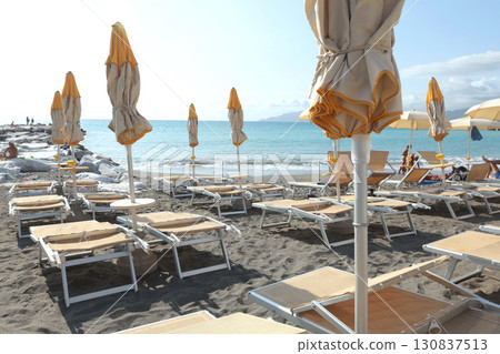 Beach umbrellas and sun loungers by sea. Sunrise in summer, vacation in Liguria, Italy. Background for text 130837513