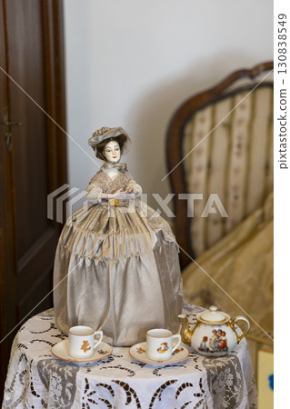 Antique porcelain doll wearing a dress and hat sitting on a table with a tea set in Jaromerice nad Rokytnou, Czechia 130838549