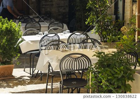 Outdoor restaurant tables with white tablecloths and black chairs in Assisi, Italy 130838622