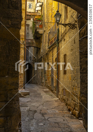 Narrow cobblestone alley in Pitigliano, Italy, featuring stone buildings and vintage street lamp Narrow cobblestone alley in Pitigliano, Italy, featuring stone buildings and vintage street lamp 130838657