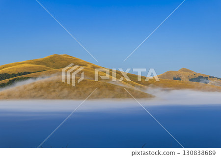 Fog covering the valley at sunrise with yellow hills in Castelluccio di Norcia, Italy Fog covering the valley at sunrise with yellow hills in Castelluccio di Norcia, Italy 130838689