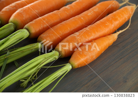 Fresh Orange Carrots with Green Tops on Wooden Surface Fresh Orange Carrots with Green Tops on Wooden Surface 130838823