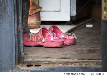 Worn Pink Rubber Clogs Placed at a Rustic Wooden Door Entrance 130838831