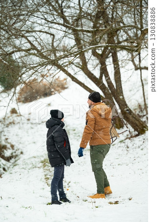 A father and son pause during a snowy winter day, carrying a sled. They're bundled in warm jackets, enjoying the winter wonderland. 130838886