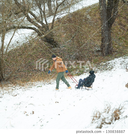 Man pulling a child on a sled through a snowy landscape. Winter fun outdoors. 130838887