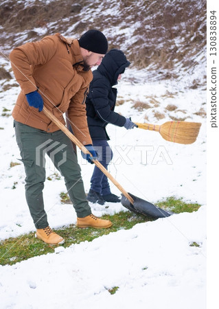 Two people shoveling snow from a grassy area on a cold winter day. Teamwork makes the snow removal easier. 130838894