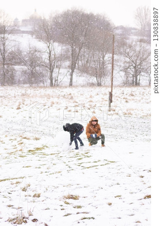 Two individuals enjoy a snowy day, playfully making snowballs in a wintry landscape. 130838897