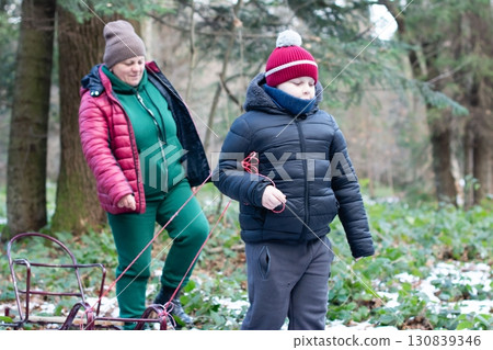 A woman and child walk through a snowy forest, pulling a sled. 130839346
