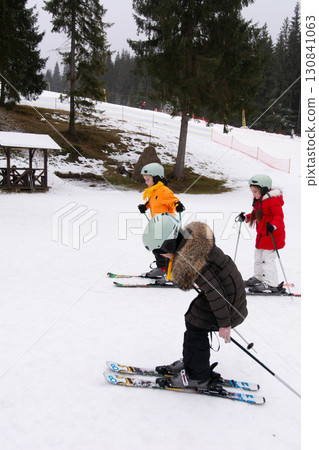 Exciting day of skiing for kids on a snowy mountain slope surrounded by evergreen trees in a winter wonderland Exciting day of skiing for kids on a snowy mountain slope surrounded by evergreen trees in a winter wonderland 130841063