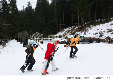 Excited children carrying skis as they head up the snowy slope on a winter afternoon in the mountains, ready for a fun day of skiing and adventure in nature 130841065