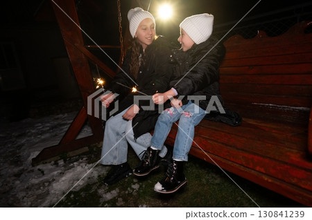 Sisters share joy and laughter while enjoying sparklers on a cold winter night at a cozy backyard setting adorned with snow Sisters share joy and laughter while enjoying sparklers on a cold winter night at a cozy backyard setting adorned with snow 130841239