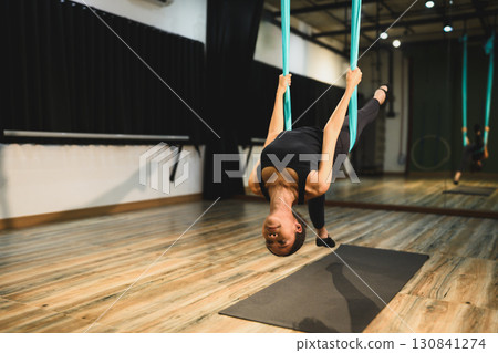 Young woman practicing aerial yoga upside down using blue hammock in fitness studio Young woman practicing aerial yoga upside down using blue hammock in fitness studio 130841274